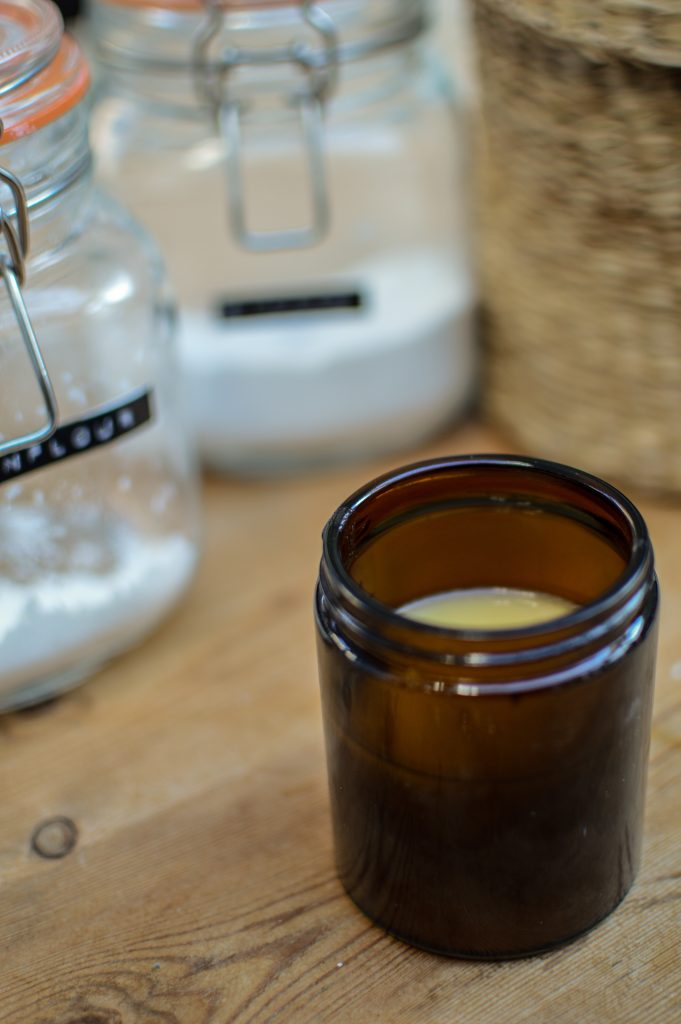 DIY deodorant in an amber glass jar on a wooden table, next to glass jars filled with cornstarch and sodium bicarbonate