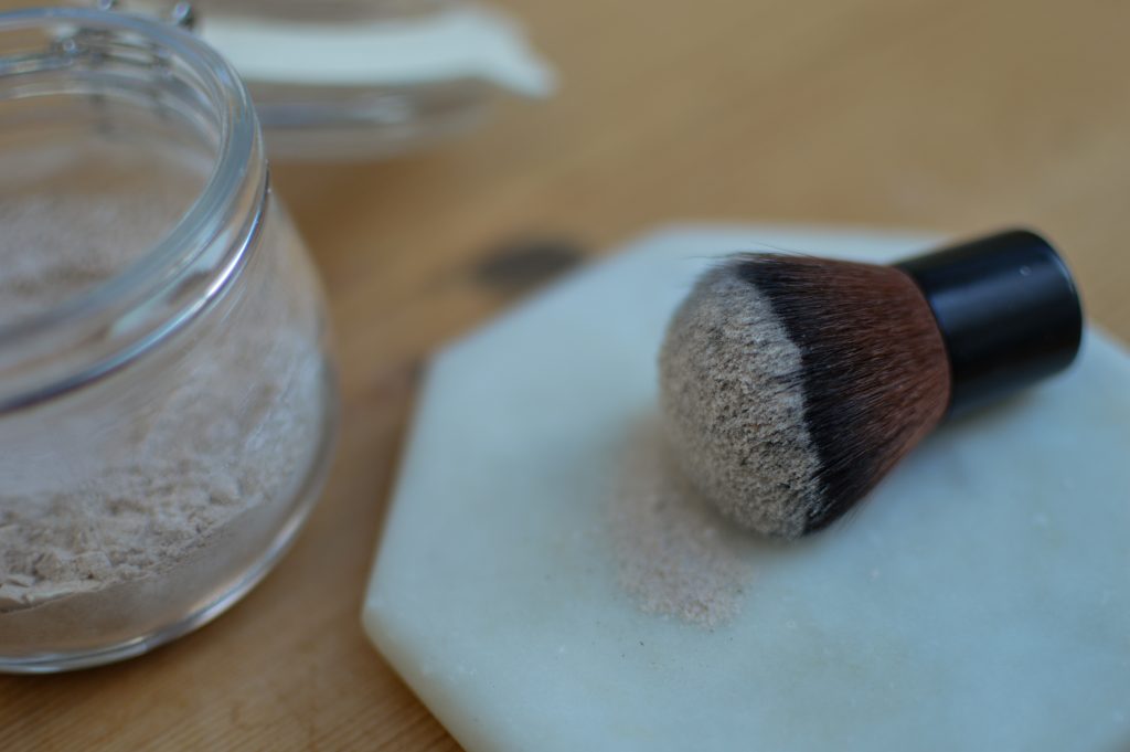 Dry shampoo on an old makeup brush next to a jar filled with dry shampoo