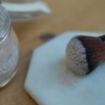 Dry shampoo on an old makeup brush next to a jar filled with dry shampoo