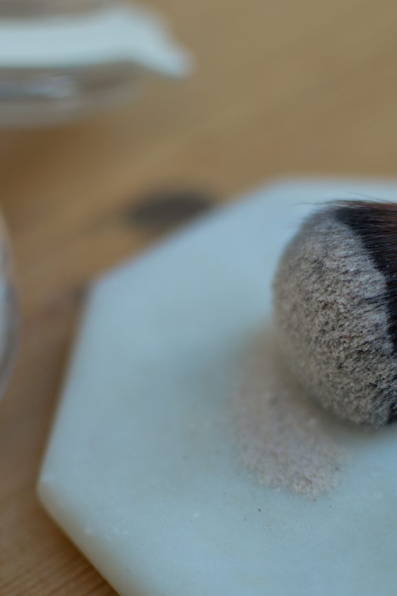 Dry shampoo on an old makeup brush next to a jar filled with dry shampoo